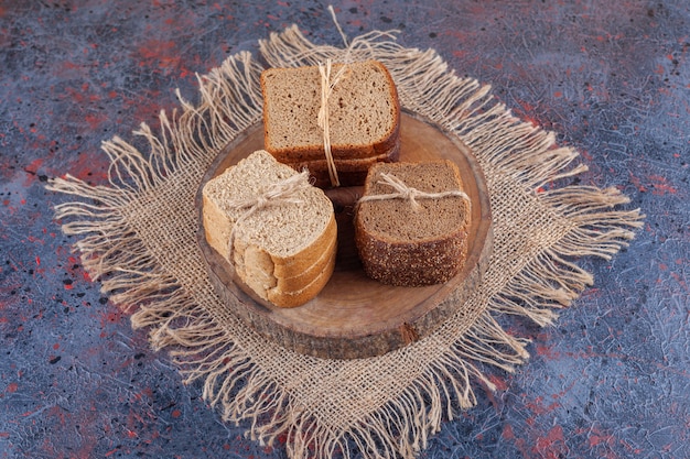 A pile of sliced bread on a board on a burlap napkin , on the blue.