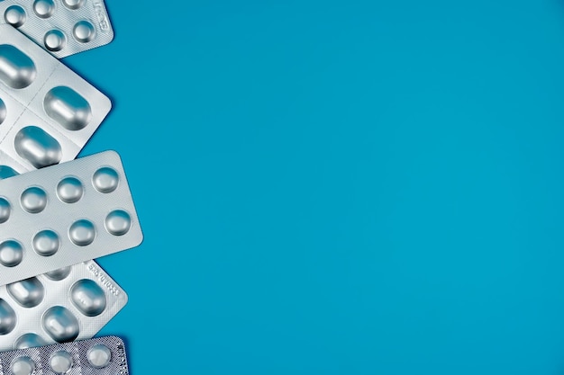 pile of tablets pill in silver blister packaging on blue background. Aluminium foil blister pack. Ph