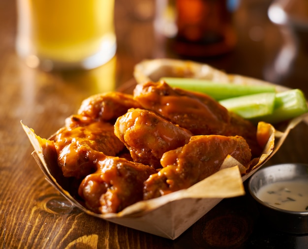 Pile of tasty buffalo chicken wings in paper tray with celery and beer