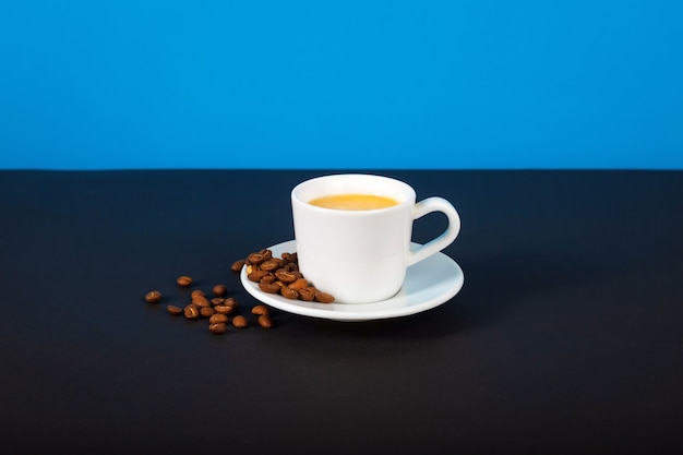 A pile of toasted coffee beans and a cup of coffee on a dark table.