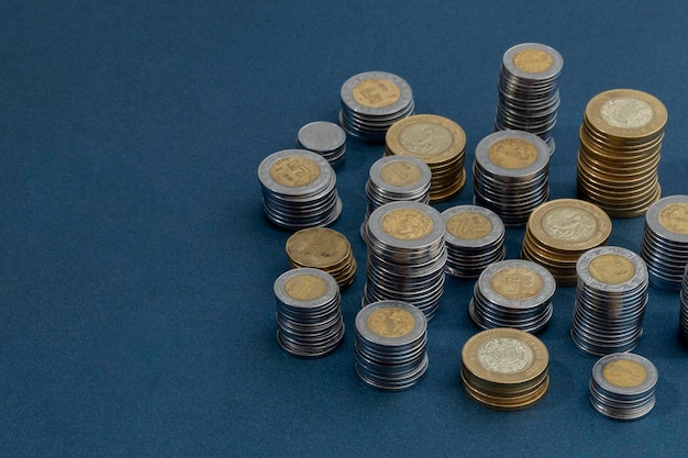 Piles of Mexican pesos coins arranged in the corner of the image with copy space and a blue background