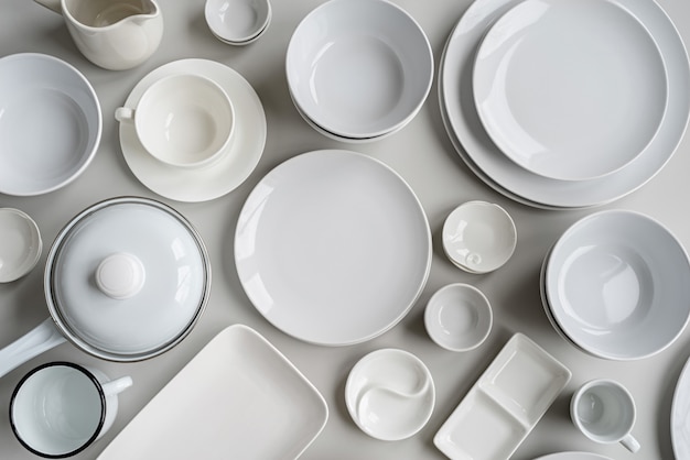 Piles of white ceramic dishes and tableware top view on gray background