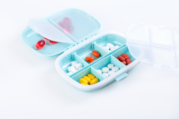 Pill box with colorful pills and vitamins Plastic blue container with cells for medicines Health concept Selective focus closeup