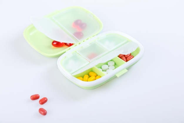 Pill box with colorful pills and vitamins Plastic green container with cells for medicines Health concept Selective focus closeup