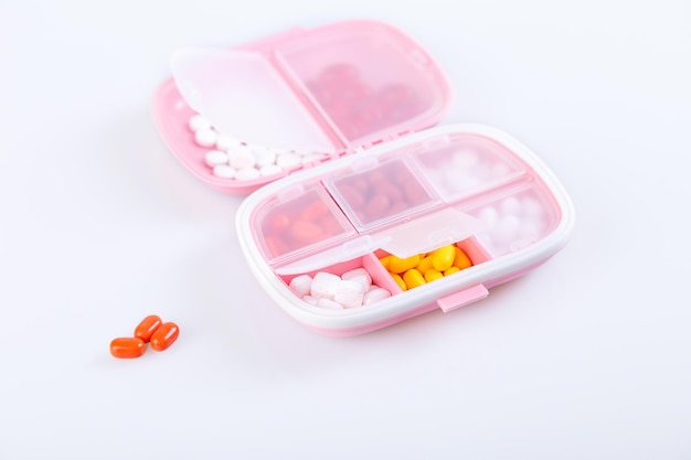 Pill box with colorful pills and vitamins Plastic pink container with cells for medicines Health concept Selective focus closeup