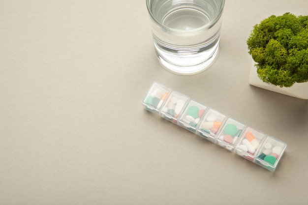 Pill box with medicaments and glass of water on grey background Space for text