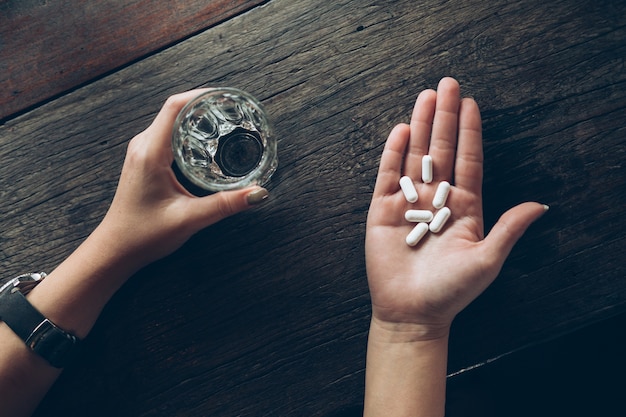 Pill of medicine in the hand with water on wooden background