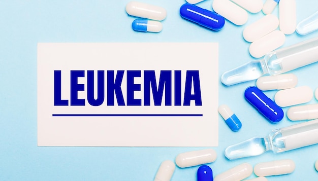 Pills, ampoules and a white card with the text LEUKEMIA on a light blue background. Medical conceptV