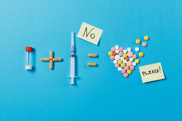 Pills bottle plus syringe needle equals medication colorful round tablets in form of heart isolated on blue background