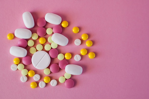 Pills of different colors and shapes on a pink background