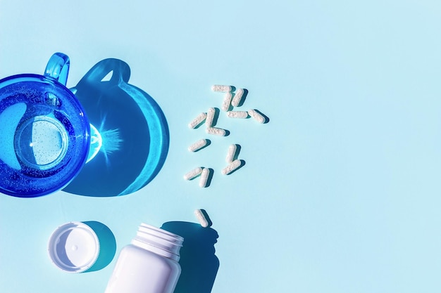 Pills and glass of water on blue background Medicine healthcare concept