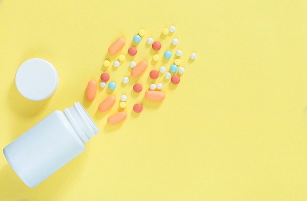 pills and pill bottles on yellow backgroundWhite pills and white bottle with copy space