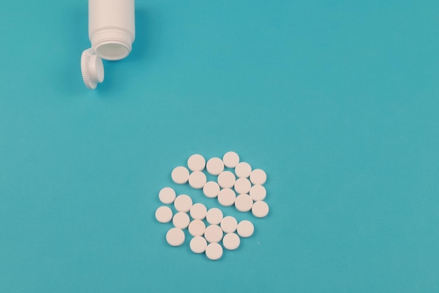 Pills spilled out of white bottle on blue background