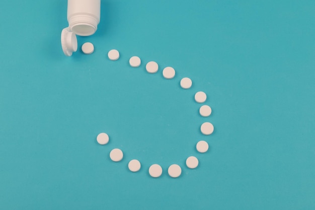 Pills spilled out of white bottle on blue background