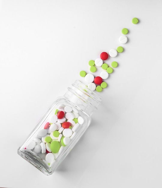 Pills spilling out from glass bottle on white background directly above