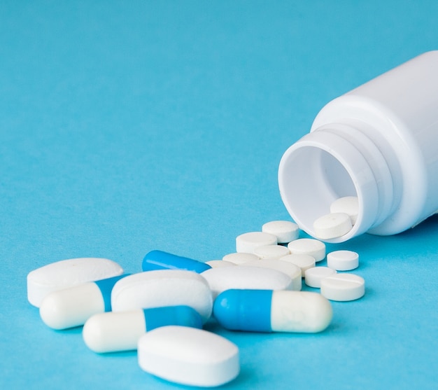 Pills spilling out of pill bottle on blue background