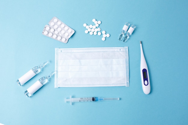 Pills spilling out of pill bottle syringe thermometer on blue background. Virus protection concept. Flat lay, top view, copy space