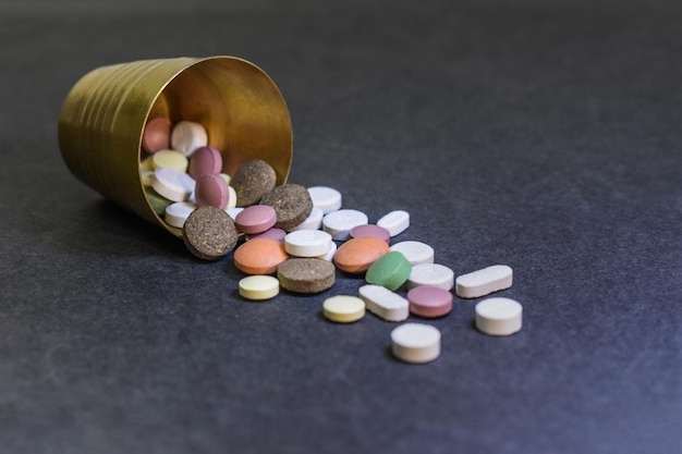 Pills spilling out of small brass glass Different types of medicine on grey background