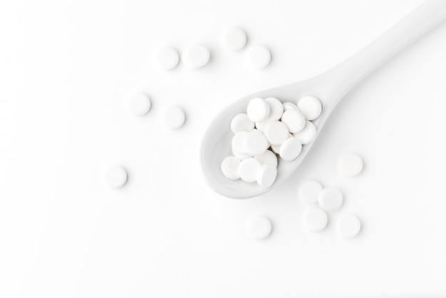 Pills on the spoon and scattered on the white surface