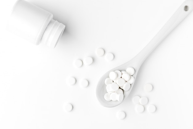 Pills on the spoon and scattered on the white surface