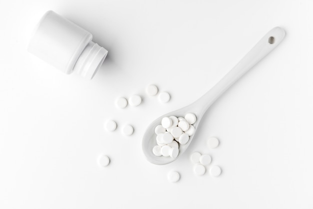 Pills on the spoon and scattered on the white surface