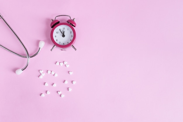 Pills, stethoscope and alarm clock on a pink  with copy space. Medical   its time to take medicine.