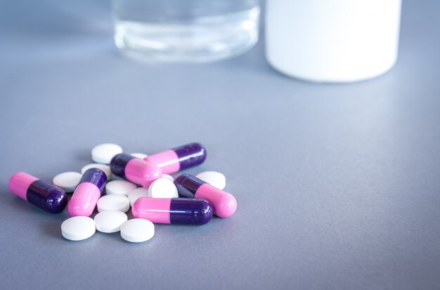 pills and tablets on grey background with bottle and glass