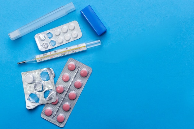 Pills and thermometer on blue background