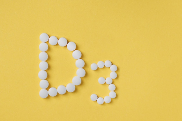 Pills of vitamin D3 on yellow background top view. Concept of vitamin d3