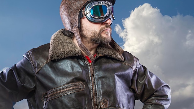 Photo pilot of the 20s with sunglasses and vintage aviator helmet. wears leather jacket, beard and expressive faces