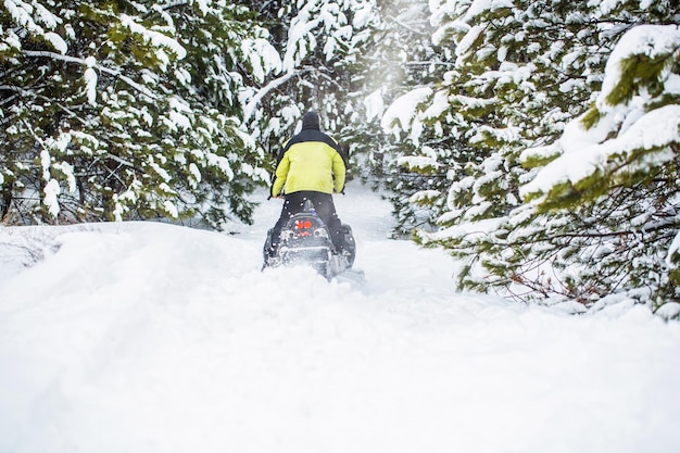 Pilot on a sports snowmobile in a mountain forest Athlete rides a snowmobile in the mountains Snowmobile in snow Concept winter sports Man is riding snowmobile in mountains