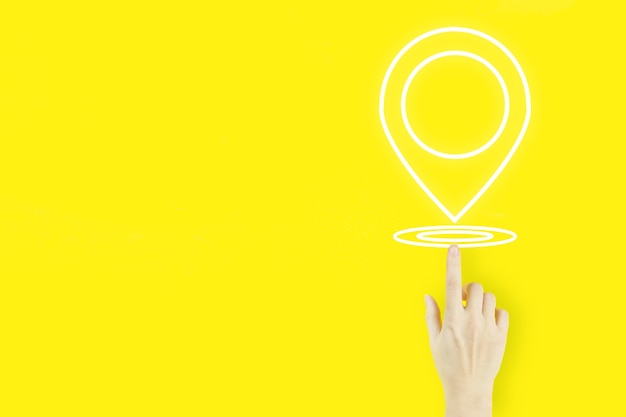 Pin address location concept. Young woman's hand finger pointing with hologram Location Marker on yellow background. Concept of Internet maps and navigation.