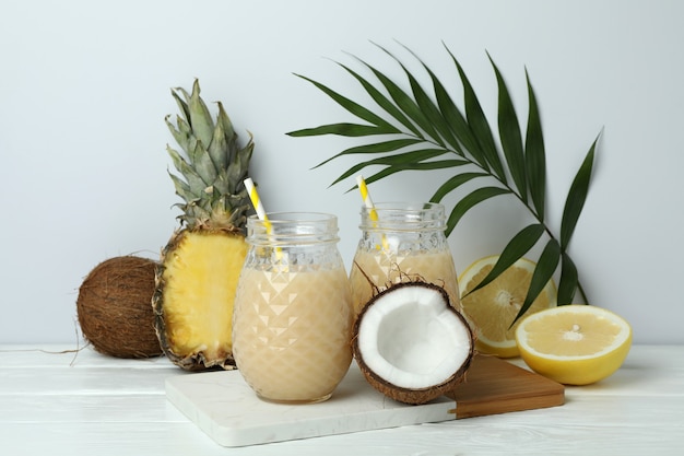 Pina colada cocktails and ingredients on white wooden table.