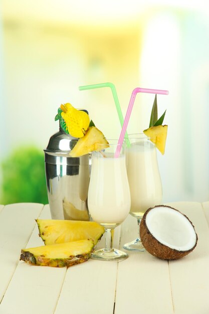 Pina colada drink in cocktail glasses and metal shaker on bright background