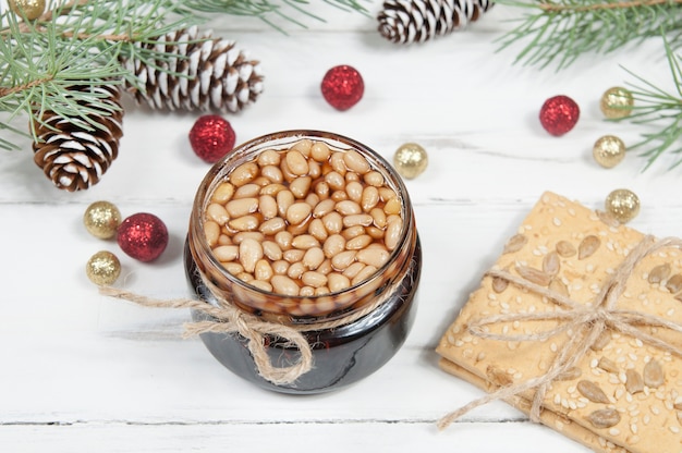 Pine nut jam in a jar and cracker cookies on a white wooden table with spruce branches and cones