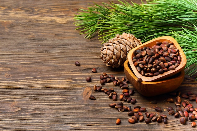 Pine nuts in a bowl and pine cone on a wooden table, place for text