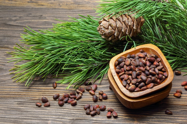 Pine nuts in a bowl and pine cone on a wooden table