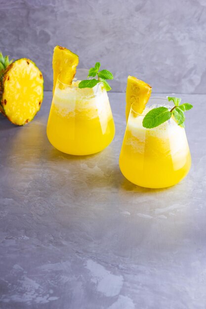 Pineapple cocktail in two glasses on a gray background Cold pineapple cocktail with mint