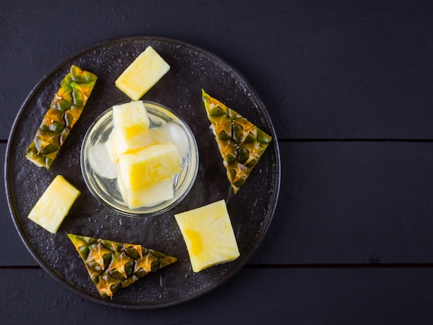 Pineapple on dark background Sliced pineapple on black plate Drink with ice and pineapple slices