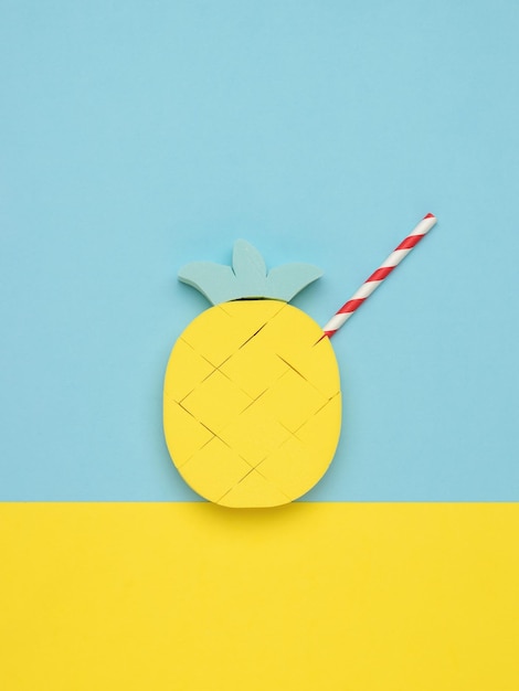 Photo pineapple figurine with a cocktail tube on a blue and yellow background. minimal summer concept.