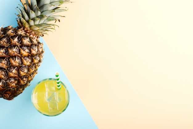 Pineapple and juice with ice in a glass, on a blue yellow Summer mood, copy space.