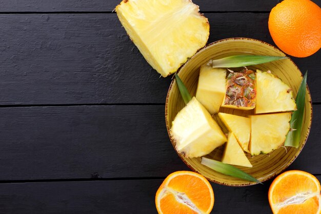 Pineapple pieces and orange halves on black wooden boards Pineapple fruit and oranges on dark background Copy space