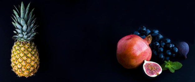 Pineapple pomegranate blue figs and grape on the black background Copy space