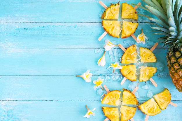 Pineapple popsicle sticks with ice on wood plank blue color.