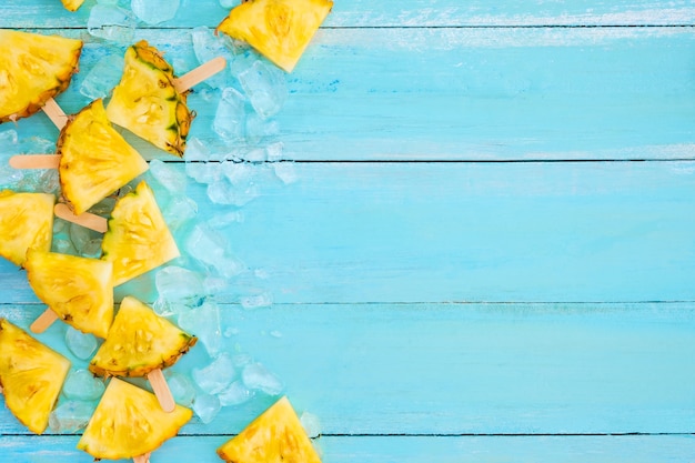 Pineapple popsicle sticks with ice on wood plank blue color