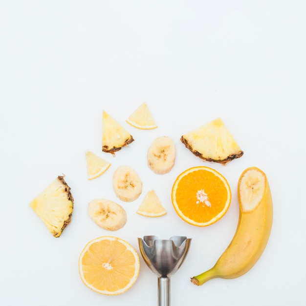 Pineapple slice; banana; orange slices with stainless steel electric hand blender on white background