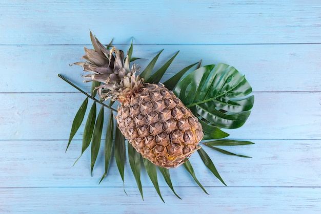 Pineapple and tropical palm leaves on blue wooden background