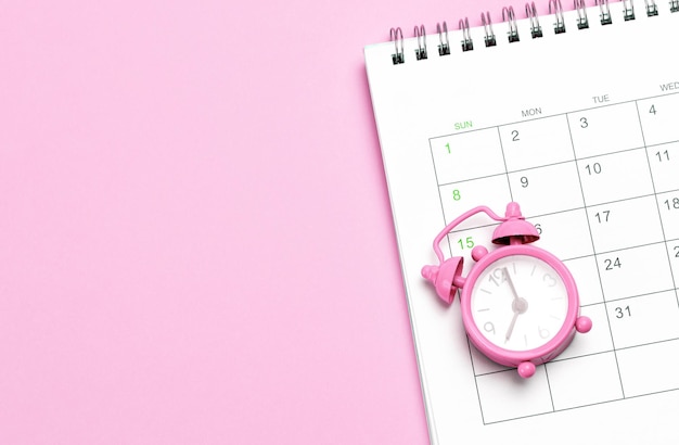 Pink alarm clock and calendar on a pink background Concept days of menstruation or menopause Template Copy space for text mockup