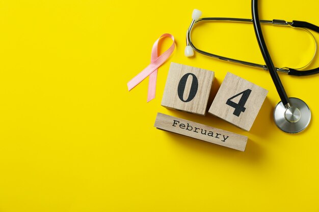 Photo pink awareness ribbon, stethoscope and 4 february on yellow background