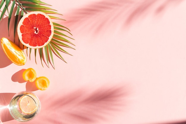 pink background with shadows summer drinks water with lemon fresh fruits with tropical tree leaf